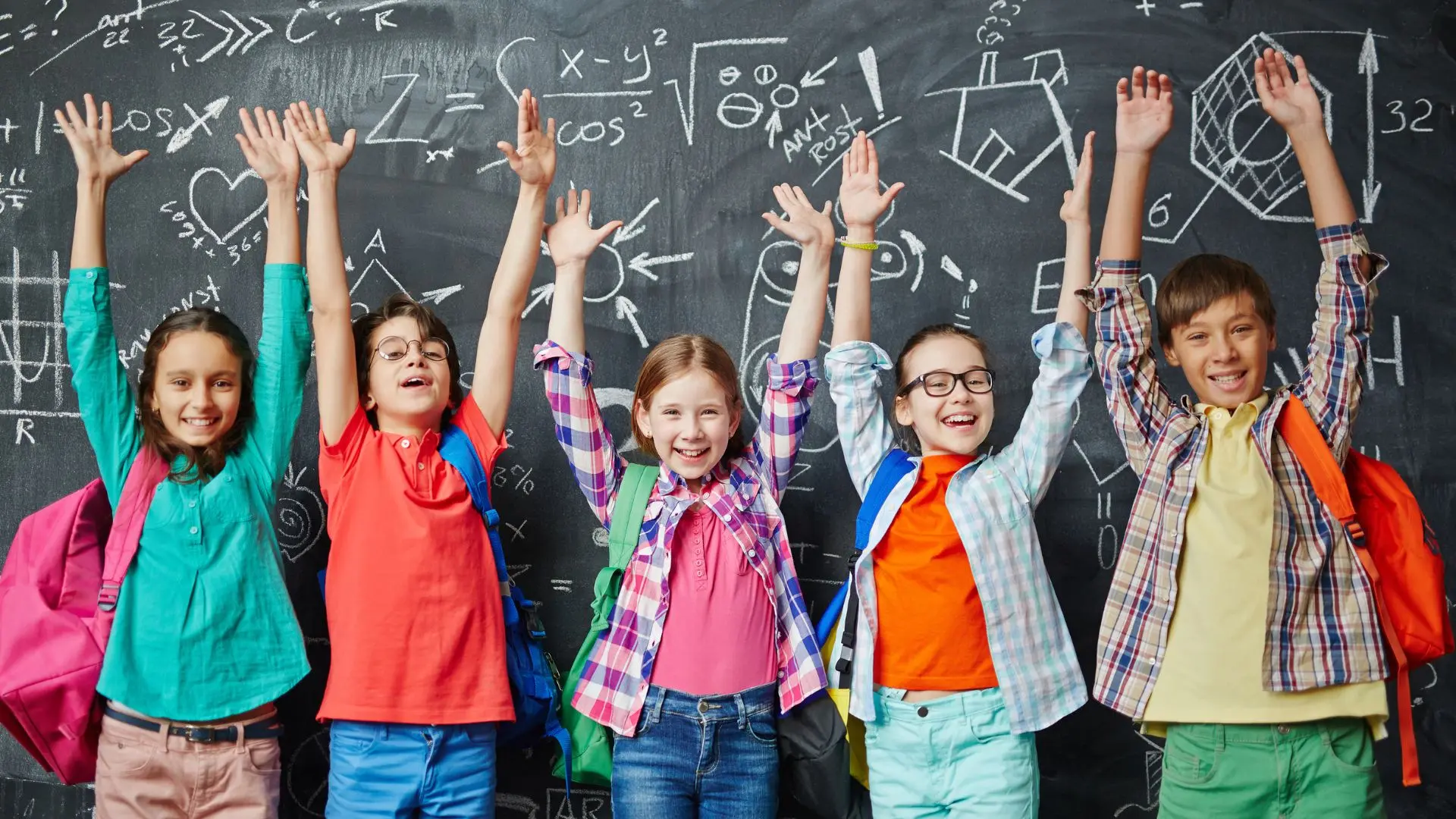 5 Schüler vor einer vollgekritzelten Wandtafel die ihre Hände in die Höhe strecken und glücklich sind.